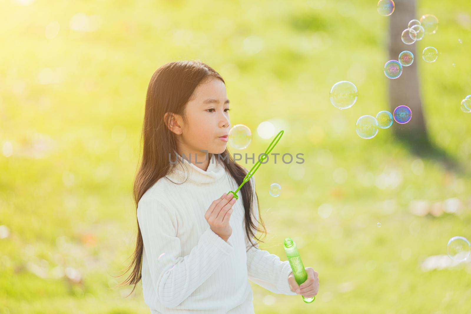 Happy Asian little cute girl child having fun and enjoying outdoor play blowing soap bubbles during in the garden park on a sunny day, summer time