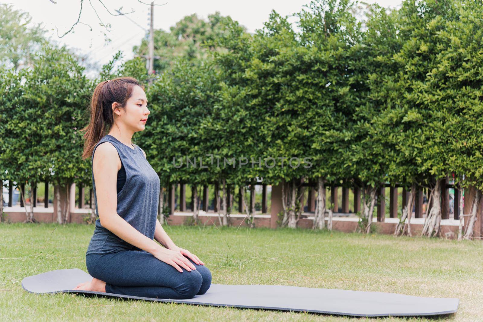 Asian young woman practicing yoga outdoors in meditate pose sitting on green grass with closed eyes in nature a field garden park, Stretching, meditation, exercise health care concept