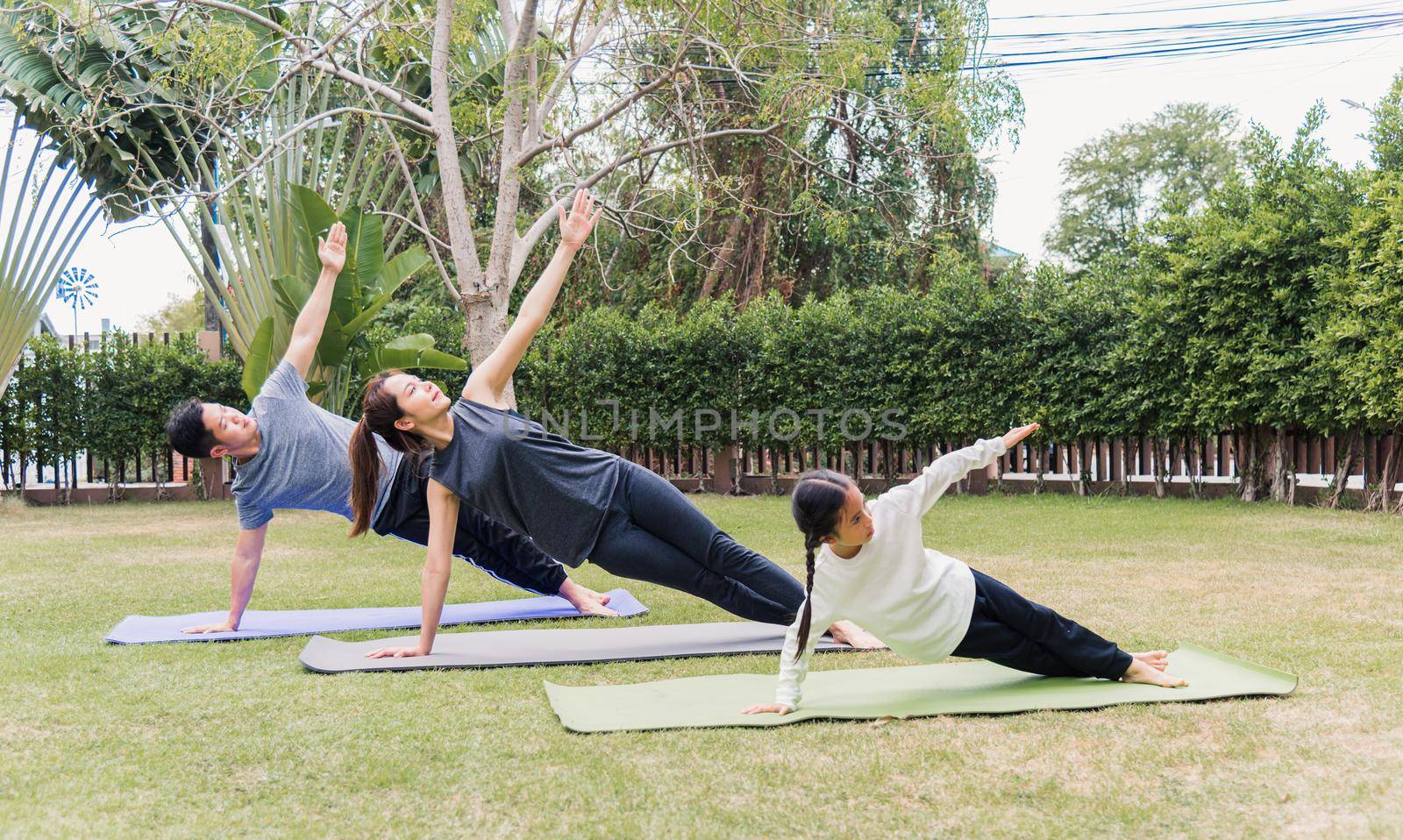 mother, father practicing doing yoga exercises with child daughter outdoors in meditate pose together by Sorapop