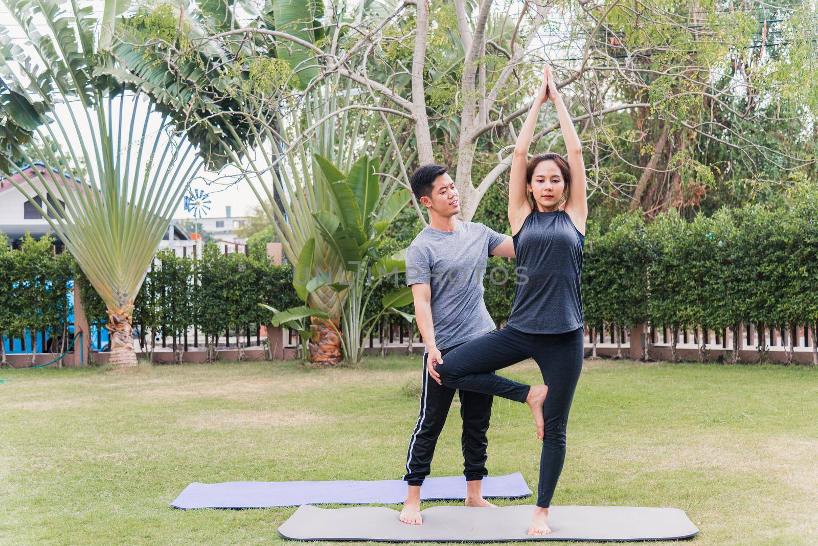 man and woman training yoga outdoors in meditate pose stand on green grass by Sorapop