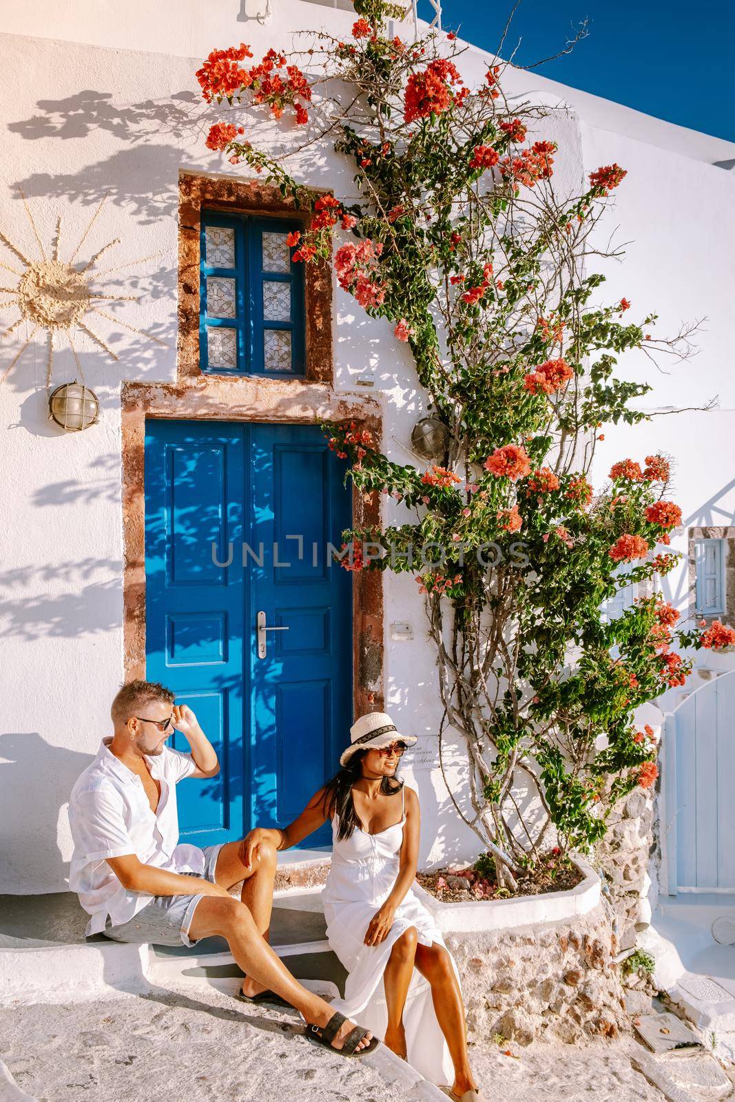 Santorini Greece, young couple on luxury vacation at the Island of Santorini watching sunrise by the blue dome church and whitewashed village of Oia Santorini Greece during sunrise, men and woman on holiday in Greece by fokkebok