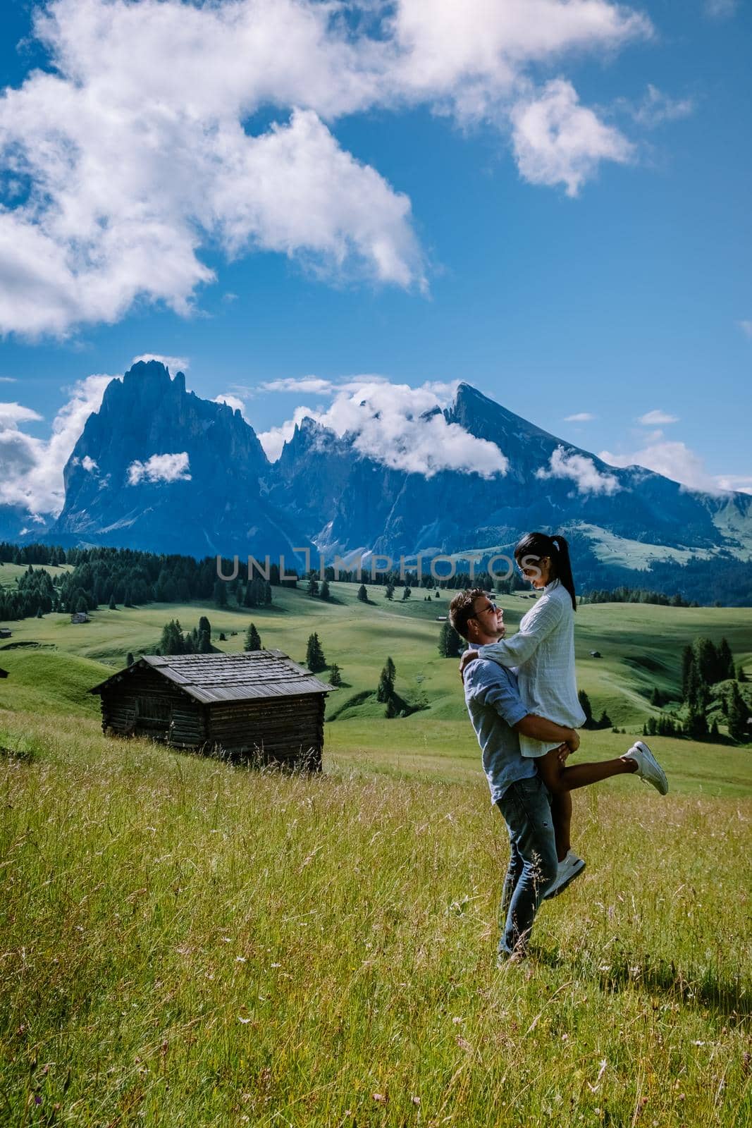 couple men and woman on vacation in the Dolomites Italy,Alpe di Siusi - Seiser Alm with Sassolungo - Langkofel mountain group in background at sunset. Yellow spring flowers and wooden chalets in Dolomites, Trentino Alto Adige, South Tyrol, Italy, Europe by fokkebok