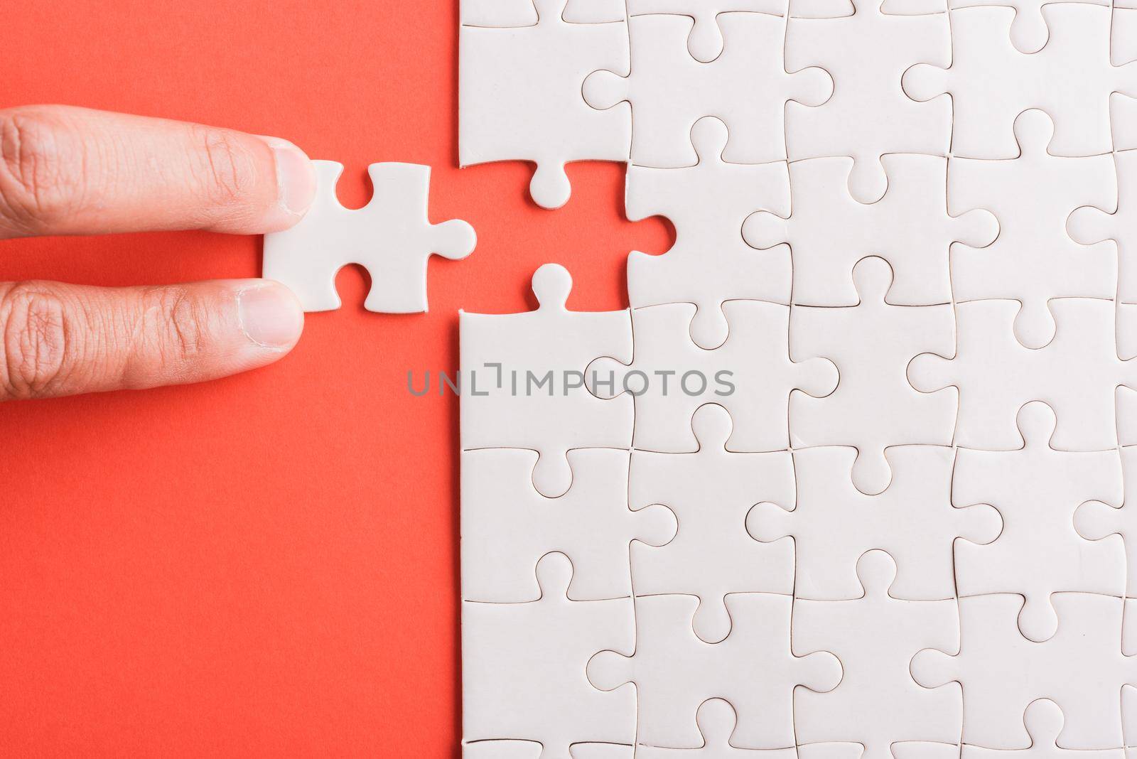 Top view flat lay of hand-holding last piece white paper jigsaw puzzle game last pieces put to place for solve problem complete mission, studio shot on a pink background, quiz calculation concept