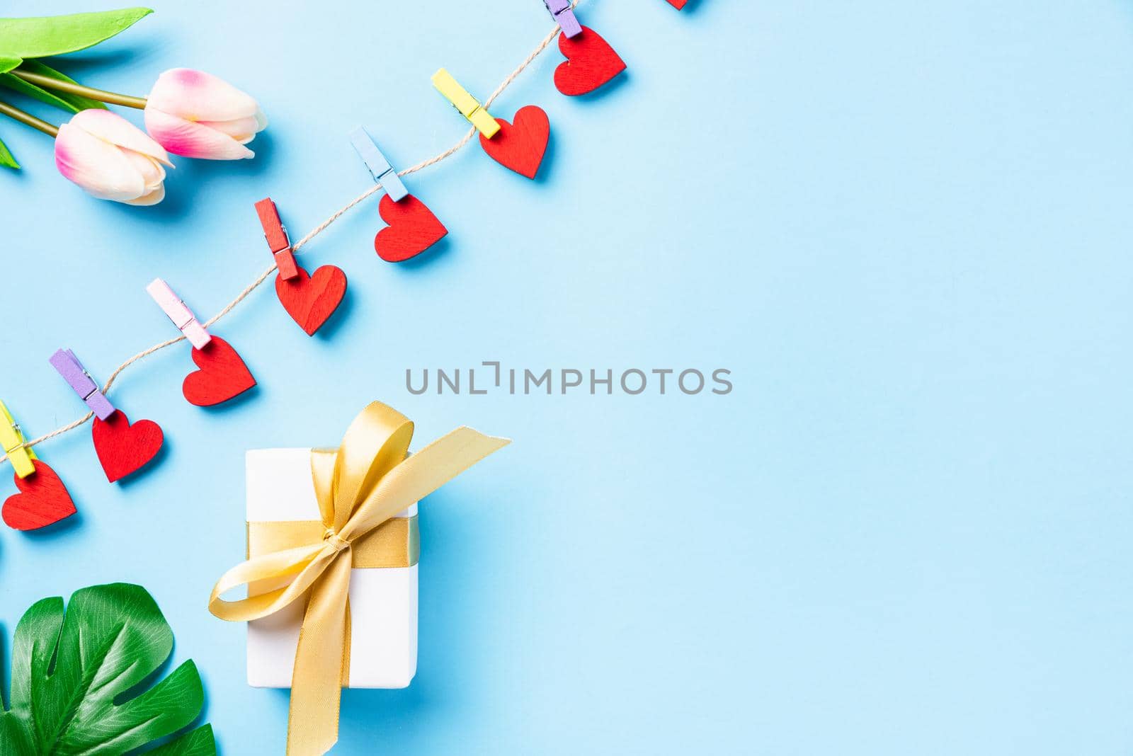 Happy Valentine's day concept. red heart-shaped valentines decoration hanging with clips for love and white gift box with golden ribbon on the rope greeting card on blue background with copy space