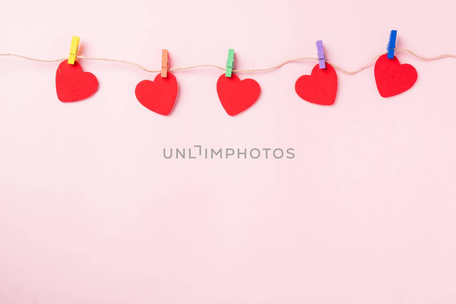 Happy Valentine's day background. red heart shaped valentines decoration hanging with paper clips on the rope for love composition greeting card isolated on pink background with copy space