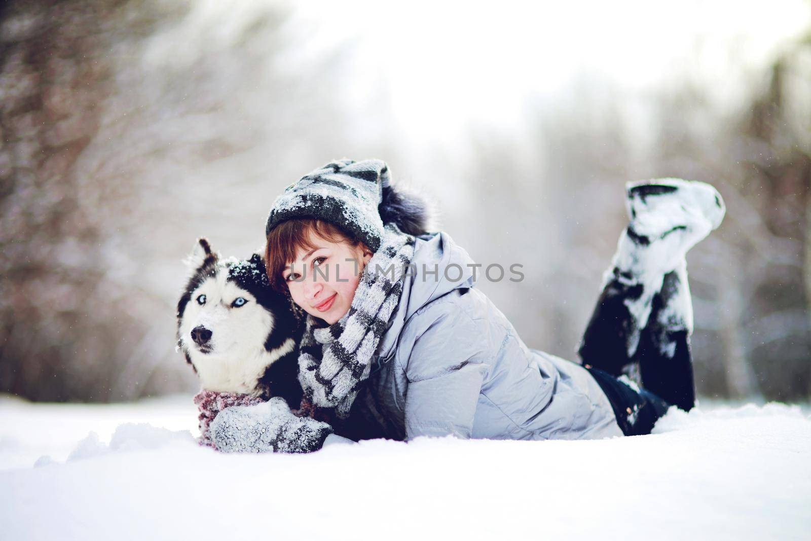 Girl lies in the snow with a siberian husky dog in the winter forest by selinsmo