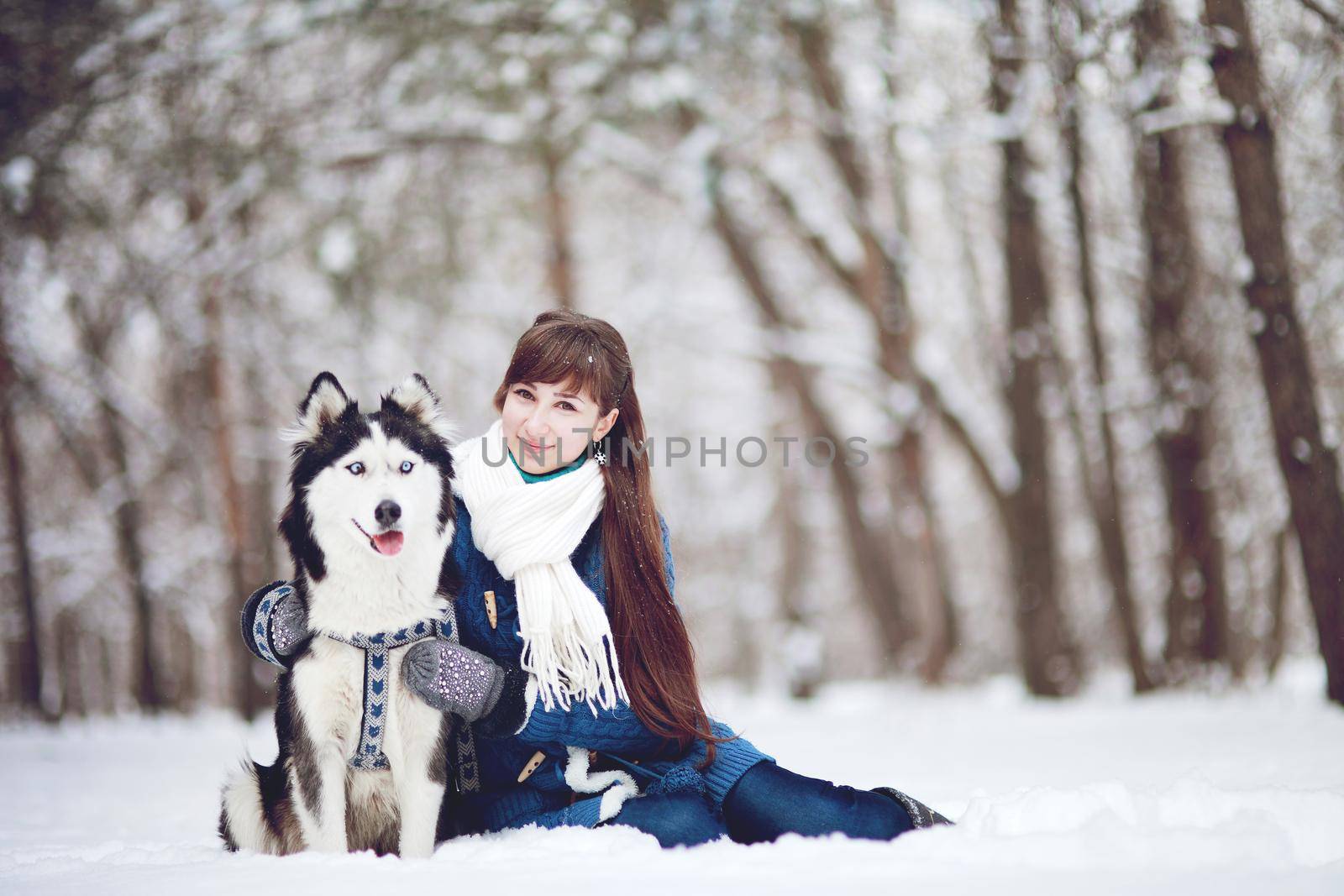 Girl sitting in the snow with a siberian husky dog in the winter forest by selinsmo