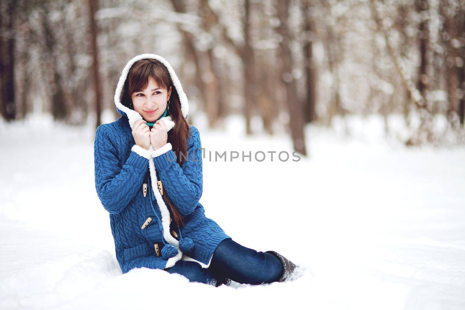 Winter portrait of a lovely girl in a blue sweater on the background of a snowy forest by selinsmo