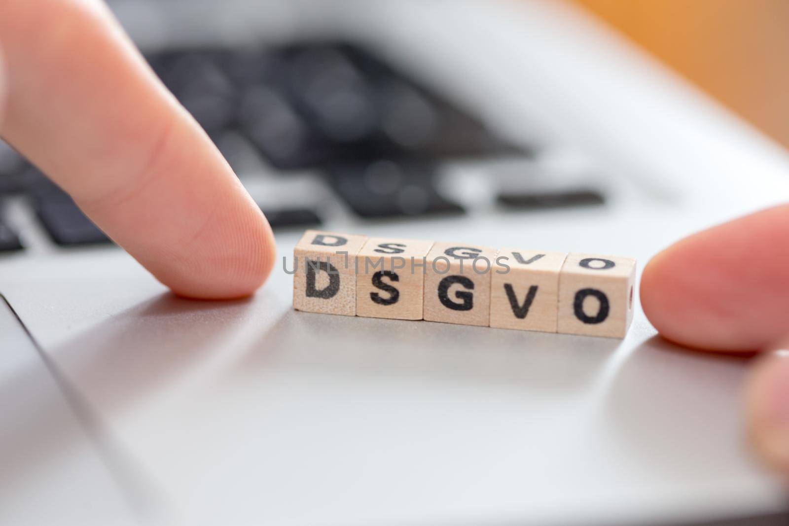 Wooden cubes with the letters “DGSVO” for Datenschutzgrundverordnung are lying on a laptop