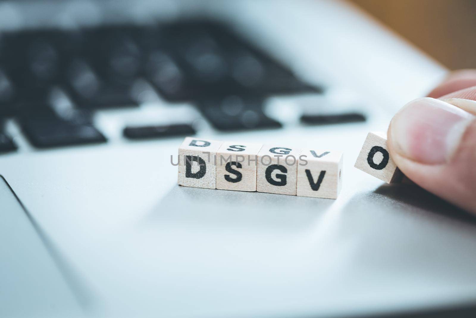 Wooden cubes with the letters “DGSVO” for Datenschutzgrundverordnung are lying on a laptop
