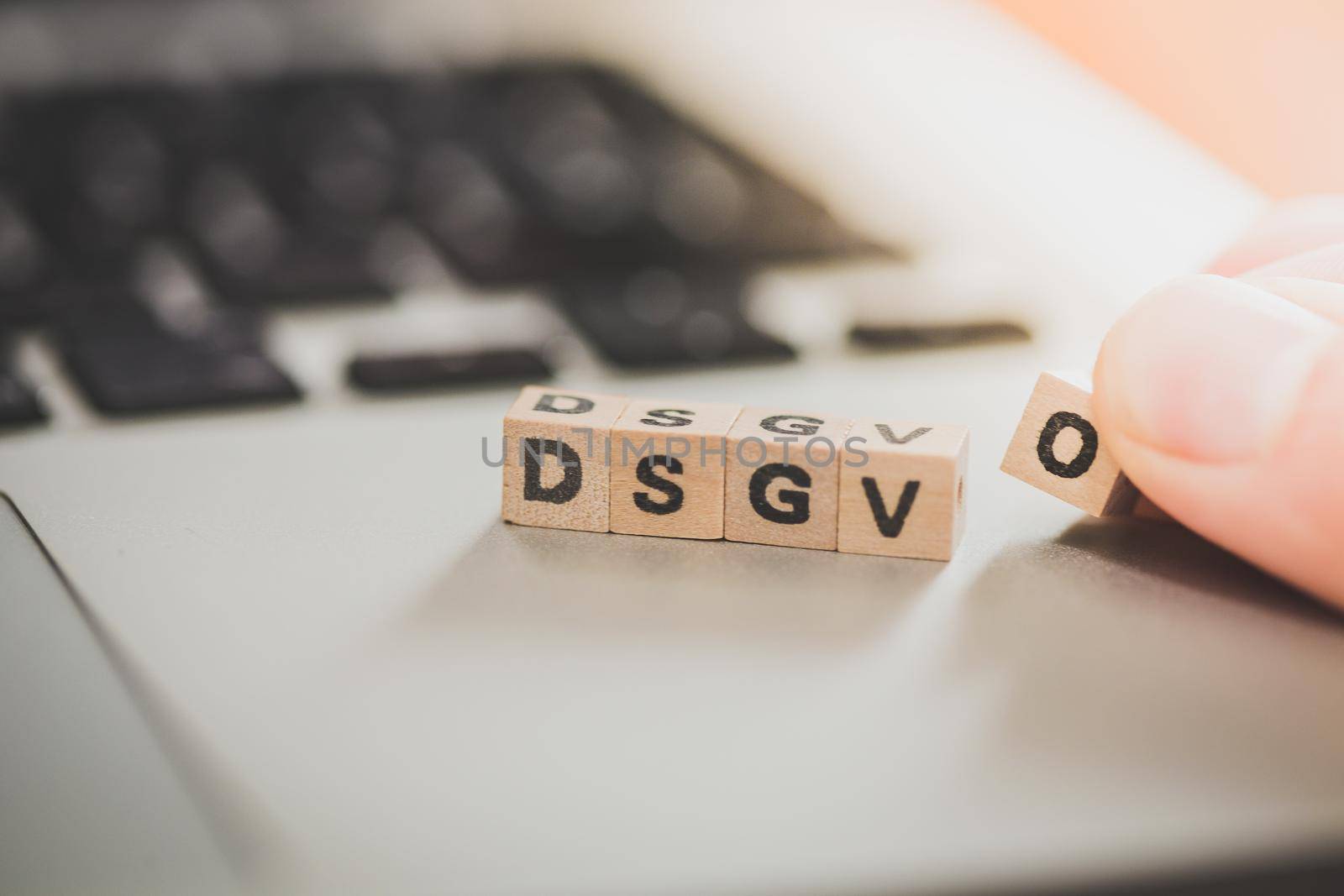 Wooden cubes with the letters “DGSVO” for Datenschutzgrundverordnung are lying on a laptop
