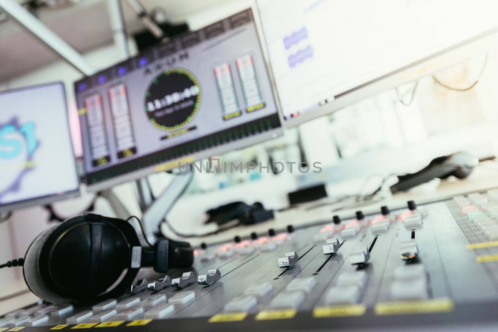 Close up picture of a soundboard in a broadcasting studio, computers in the blurry background