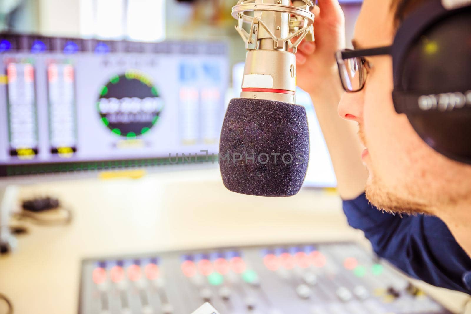 Radio moderator is sitting in a modern broadcasting studio and talking into the microphone by Daxenbichler