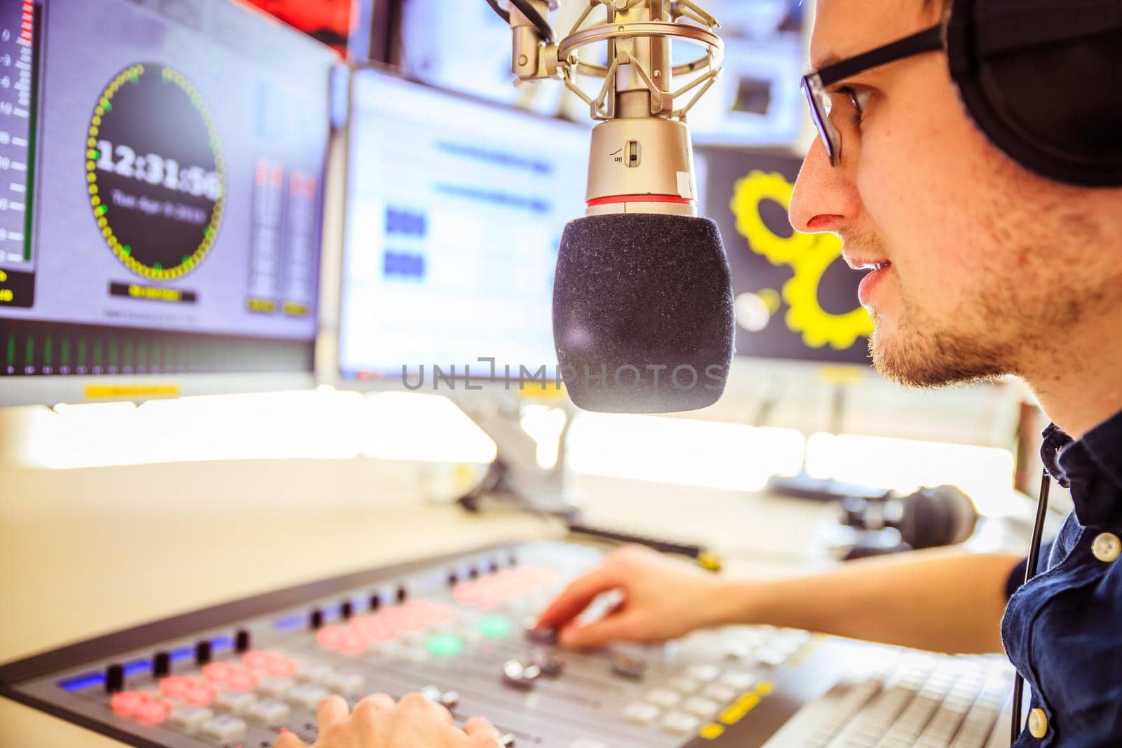 Radio moderator is sitting in a modern broadcasting studio and talking into the microphone by Daxenbichler