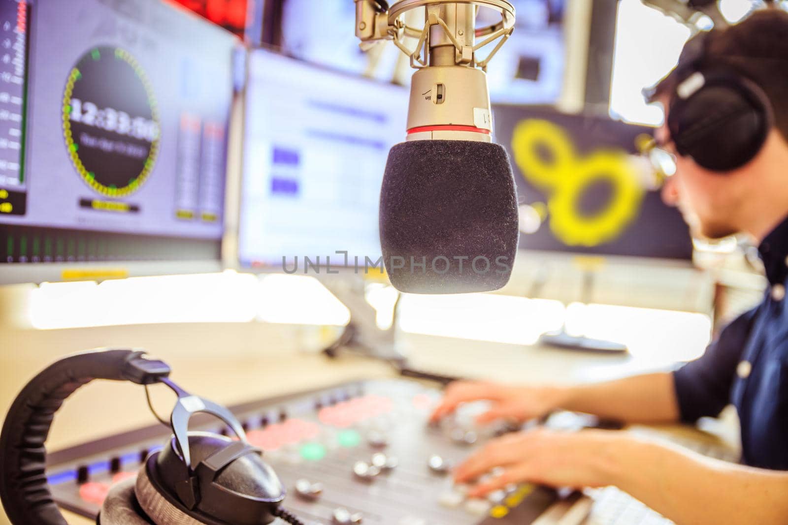 Radio moderator is sitting in a modern broadcasting studio and talking into the microphone by Daxenbichler