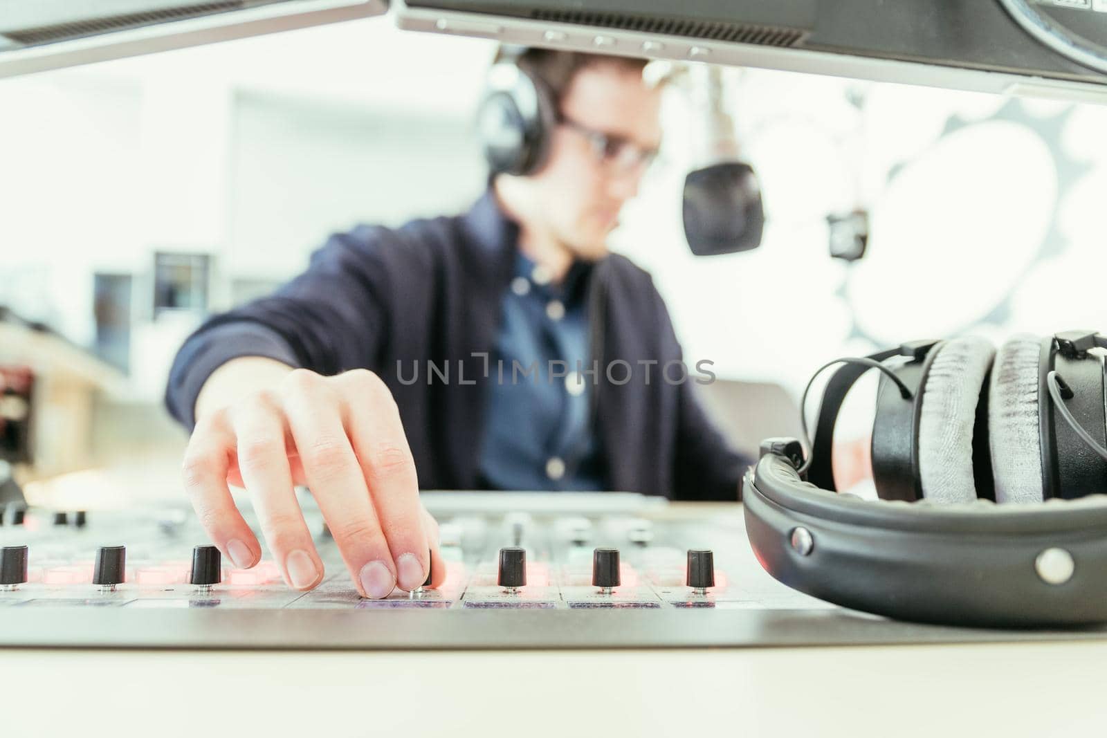 Radio moderator is sitting in a modern broadcasting studio and talking into the microphone by Daxenbichler