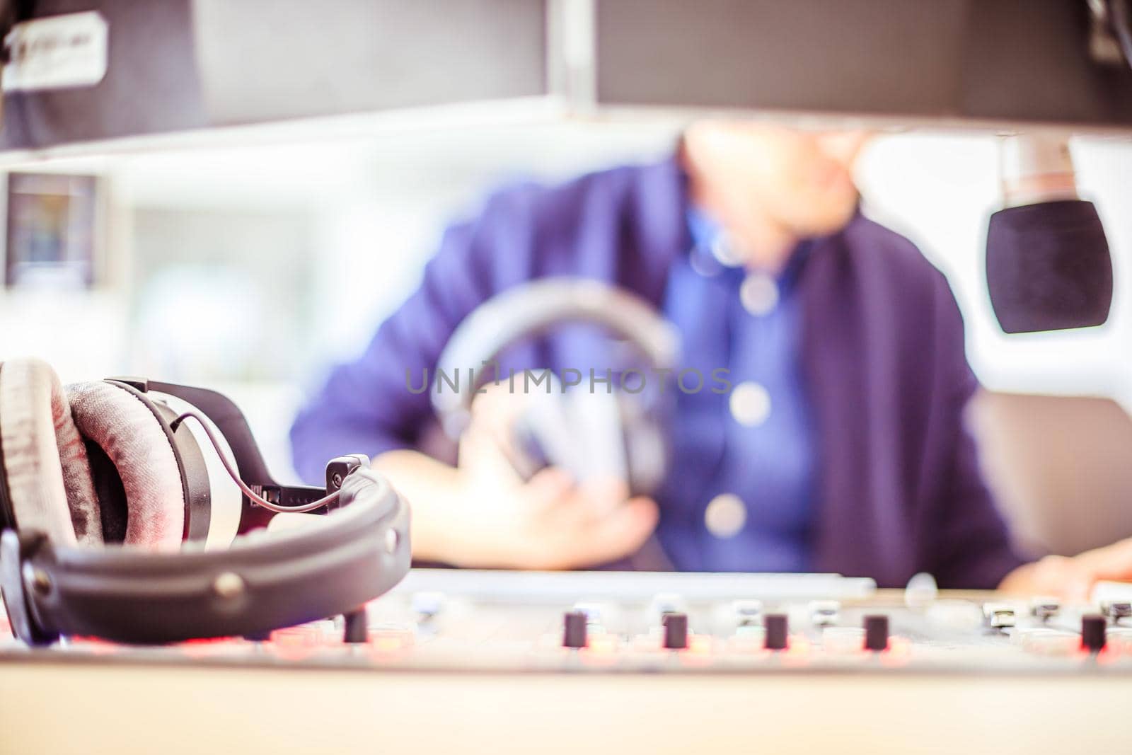 Radio moderator is sitting in a modern broadcasting studio and talking into the microphone by Daxenbichler