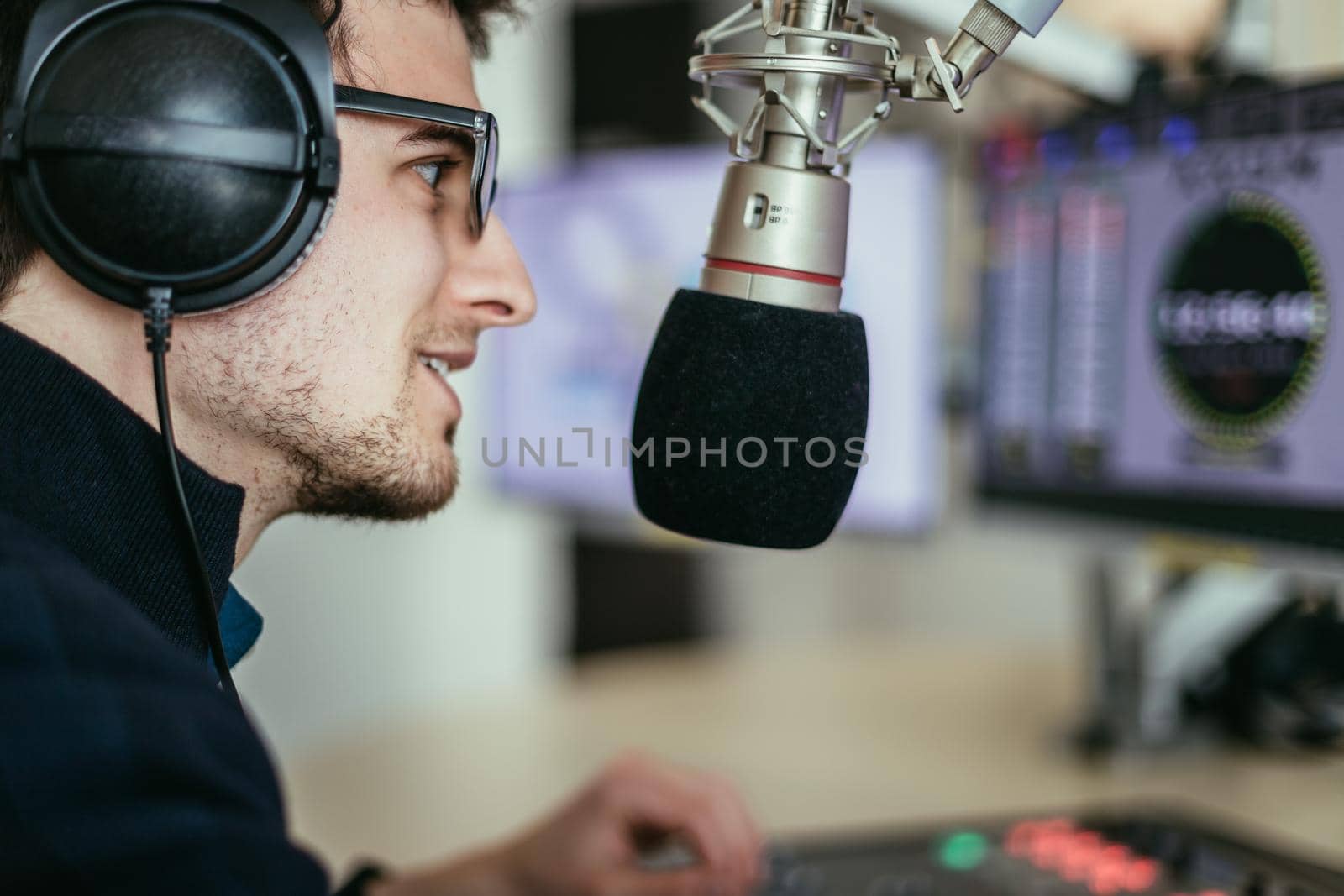 Radio moderator is sitting in a modern broadcasting studio and talking into the microphone by Daxenbichler