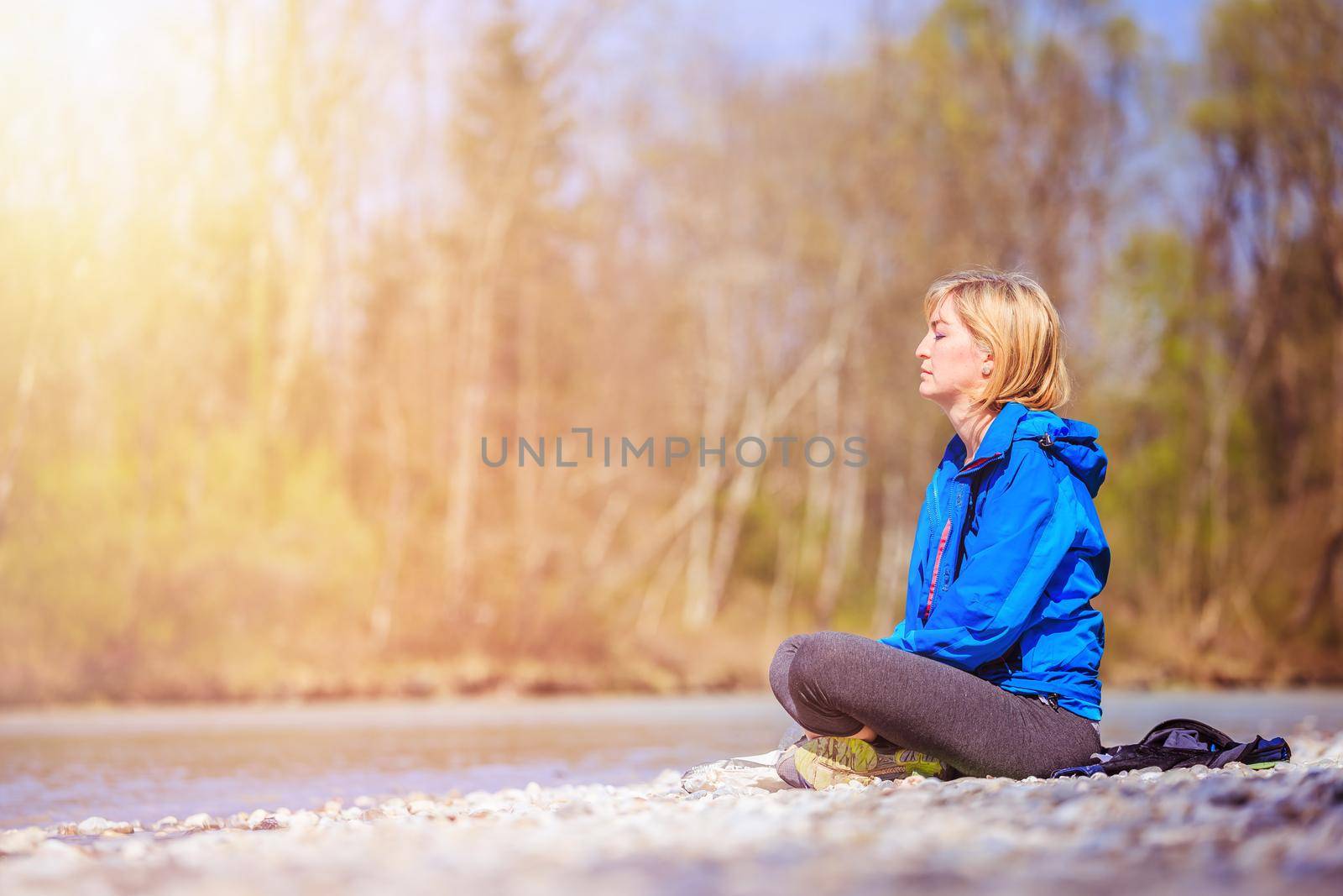Meditation and relaxation: Woman is meditating outdoors on a pebble beach. Enjoying the morning sun. by Daxenbichler