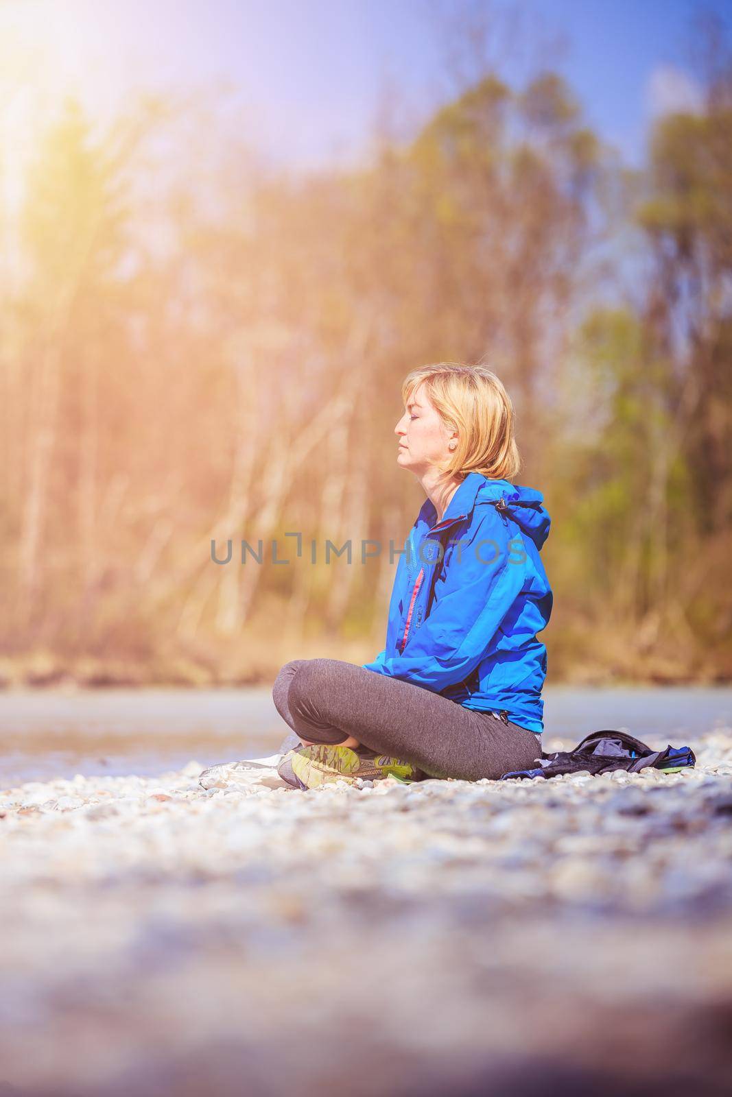 Woman is sitting on a pebble beach and doing meditation. Morning sun.