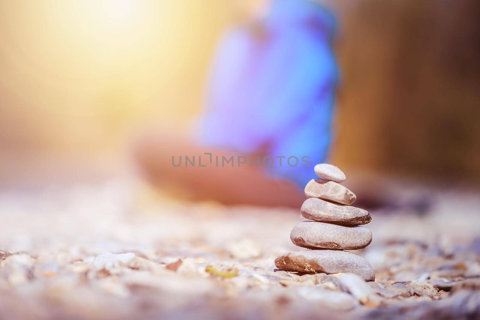 Cairn on a pebble beach, meditating woman in the background. Morning sun.