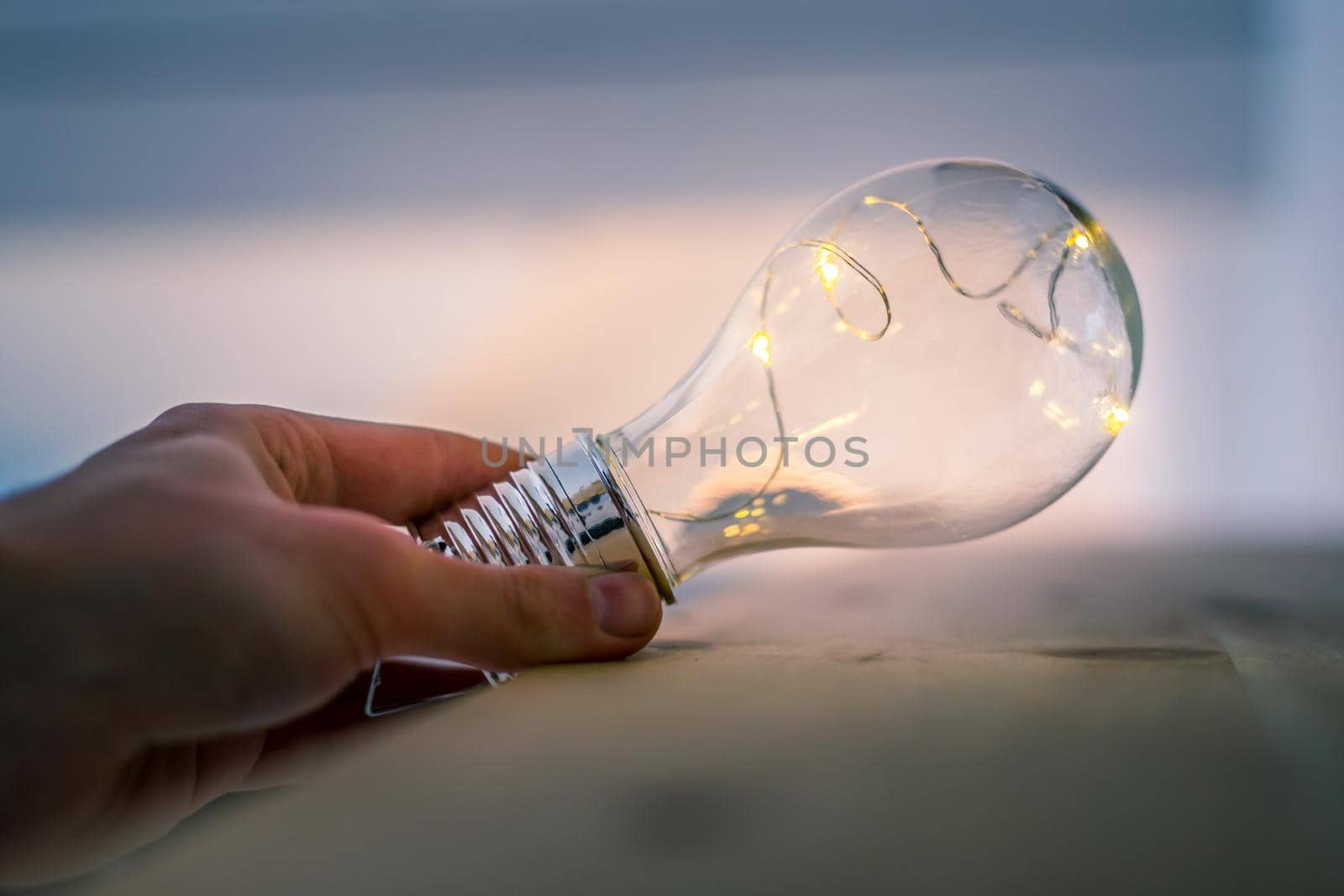 Hands are holding a LED lightbulb over the wooden floor. Symbol for ideas and innovation. Window