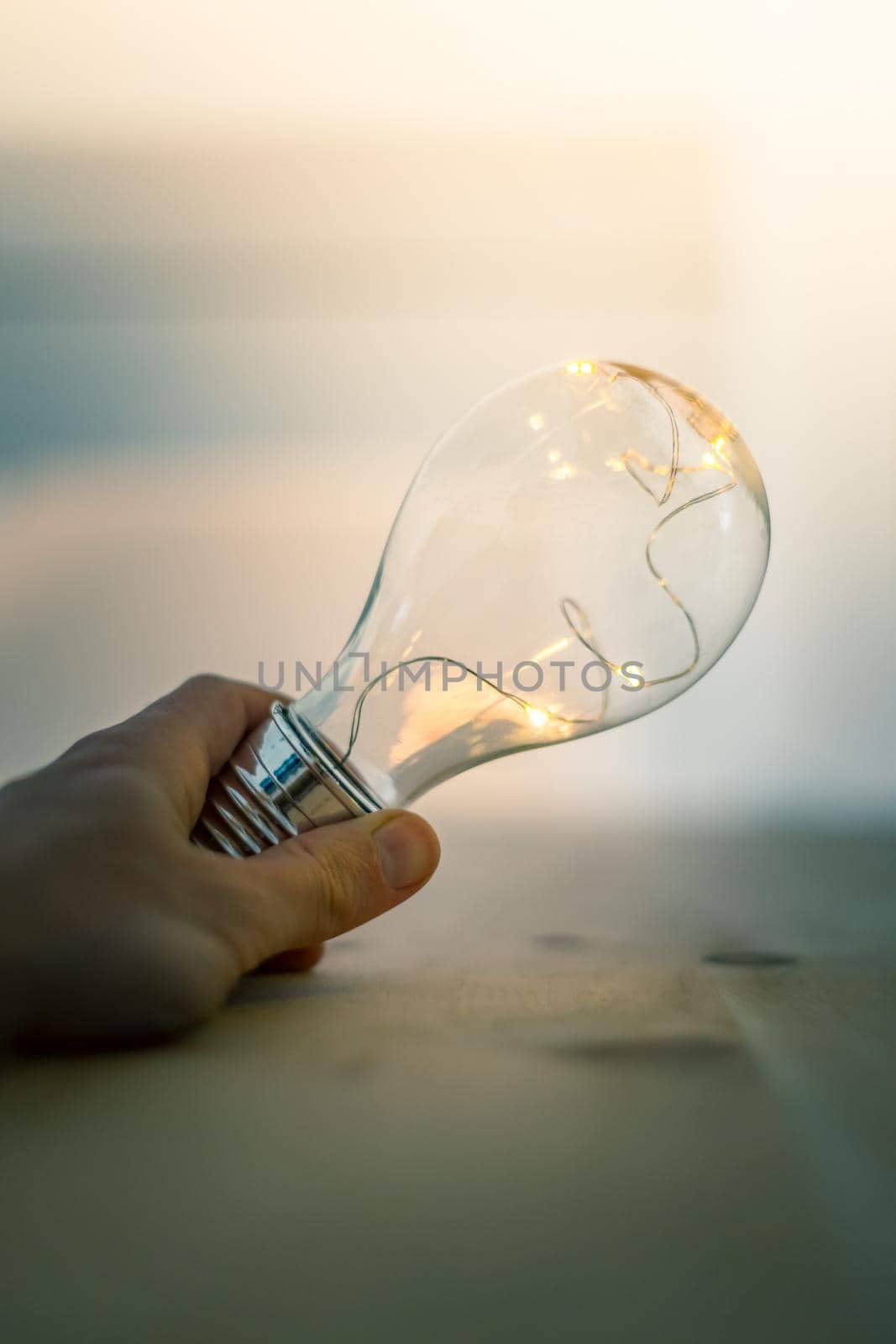 Hands are holding a LED lightbulb over the wooden floor. Symbol for ideas and innovation. Window