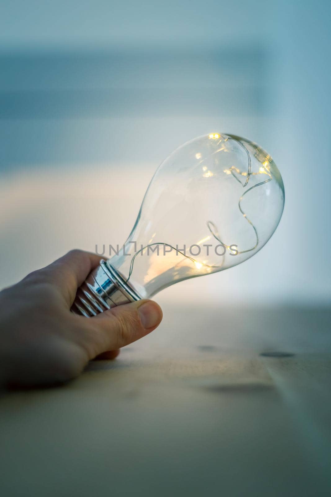 Hands are holding a LED lightbulb over the wooden floor. Symbol for ideas and innovation. Window