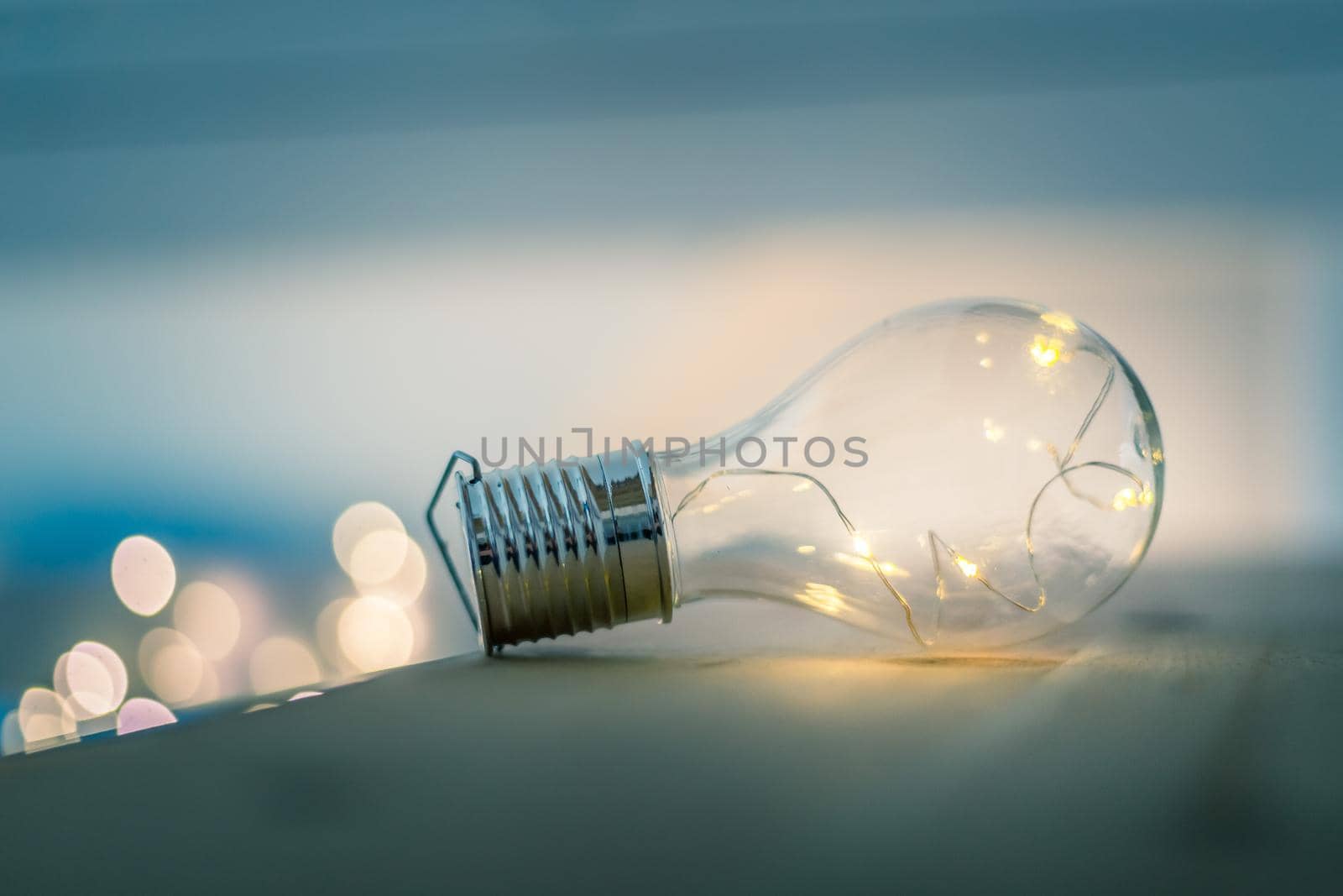 LED light bulb is lying on a wooden table. Symbol for ideas and innovation. Spot lights in the blurry background.