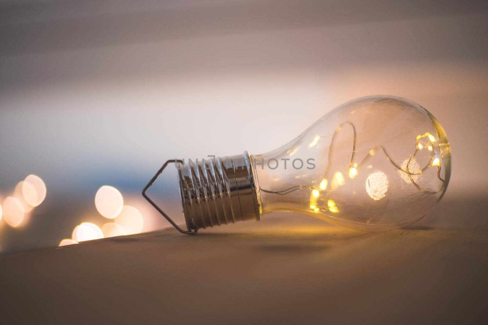 LED light bulb is lying on a wooden table. Symbol for ideas and innovation. Spot lights in the blurry background.