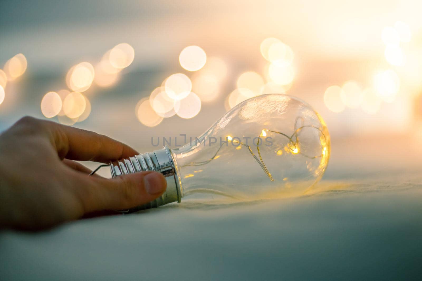 LED light bulb is lying in the bed, hands touching. Symbol for ideas and innovation. Spot lights in the blurry background.