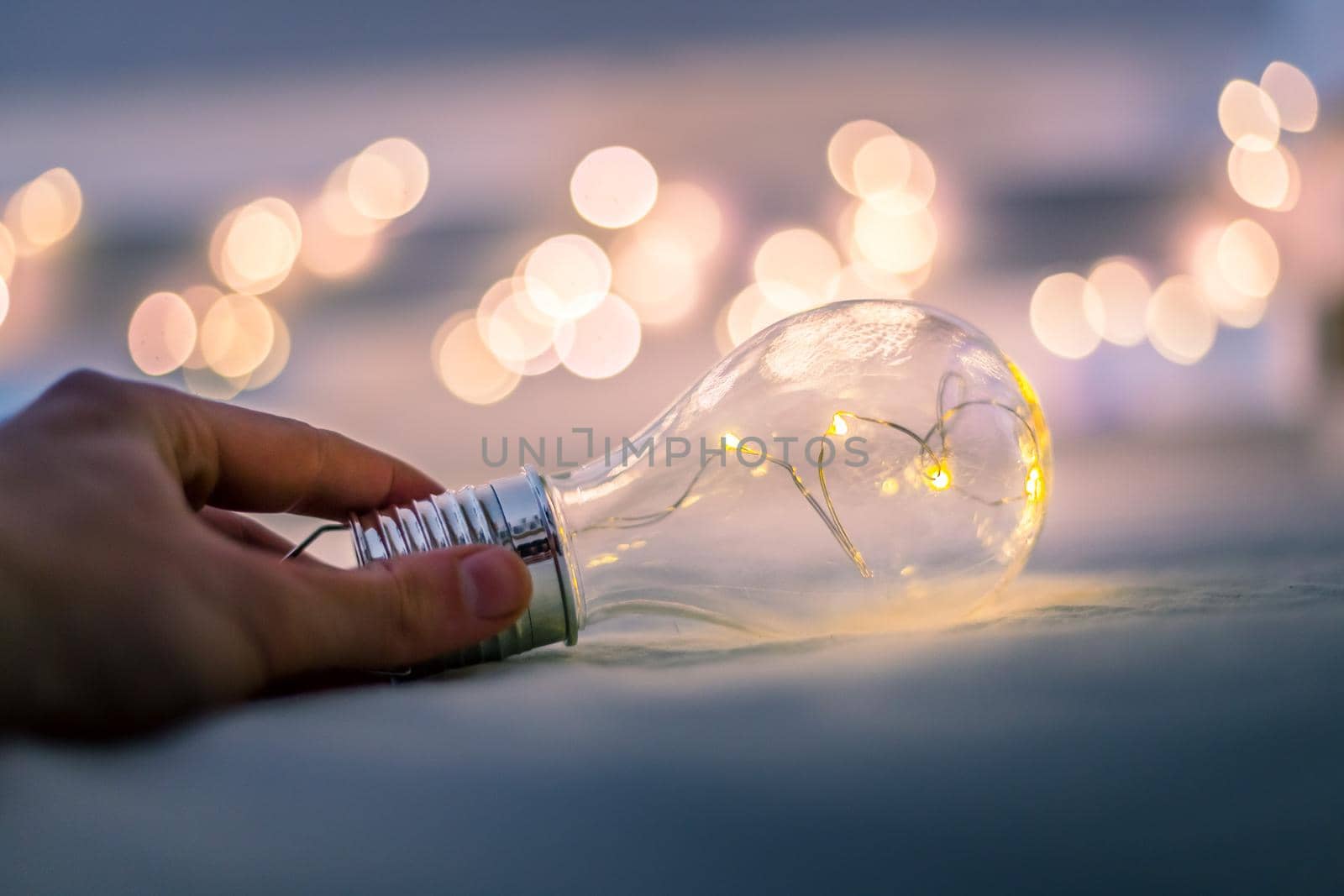 LED light bulb is lying in the bed, hands touching. Symbol for ideas and innovation. Spot lights in the blurry background.
