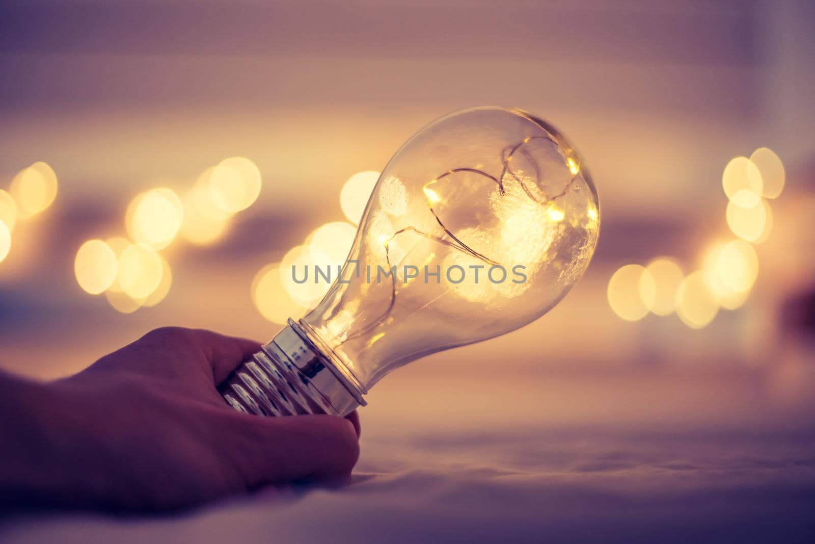 LED light bulb is lying in the bed, hands touching. Symbol for ideas and innovation. Spot lights in the blurry background.