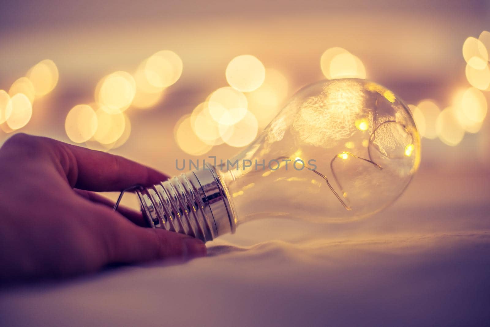 LED light bulb is lying in the bed, hands touching. Symbol for ideas and innovation. Spot lights in the blurry background.