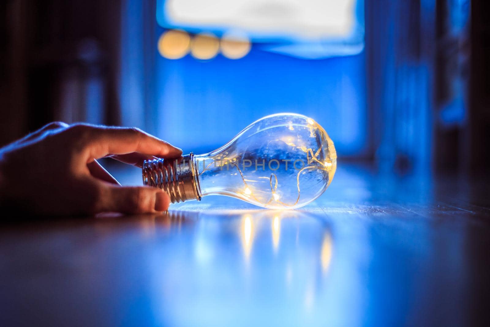Hands are holding a LED lightbulb over the wooden floor. Symbol for ideas and innovation. Window and light in the blurry background.