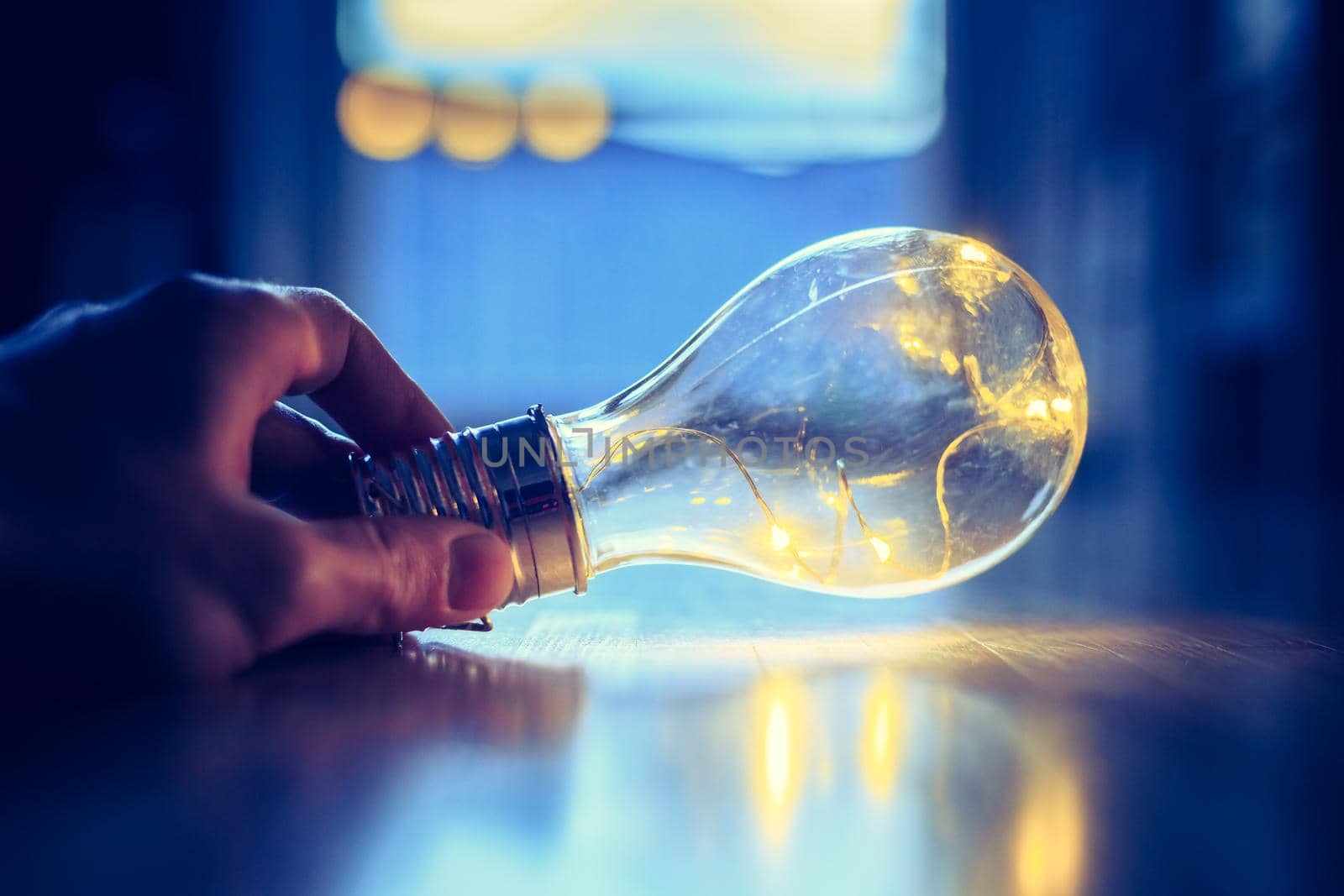 Hands are holding a LED lightbulb over the wooden floor. Symbol for ideas and innovation. Window and light in the blurry background.