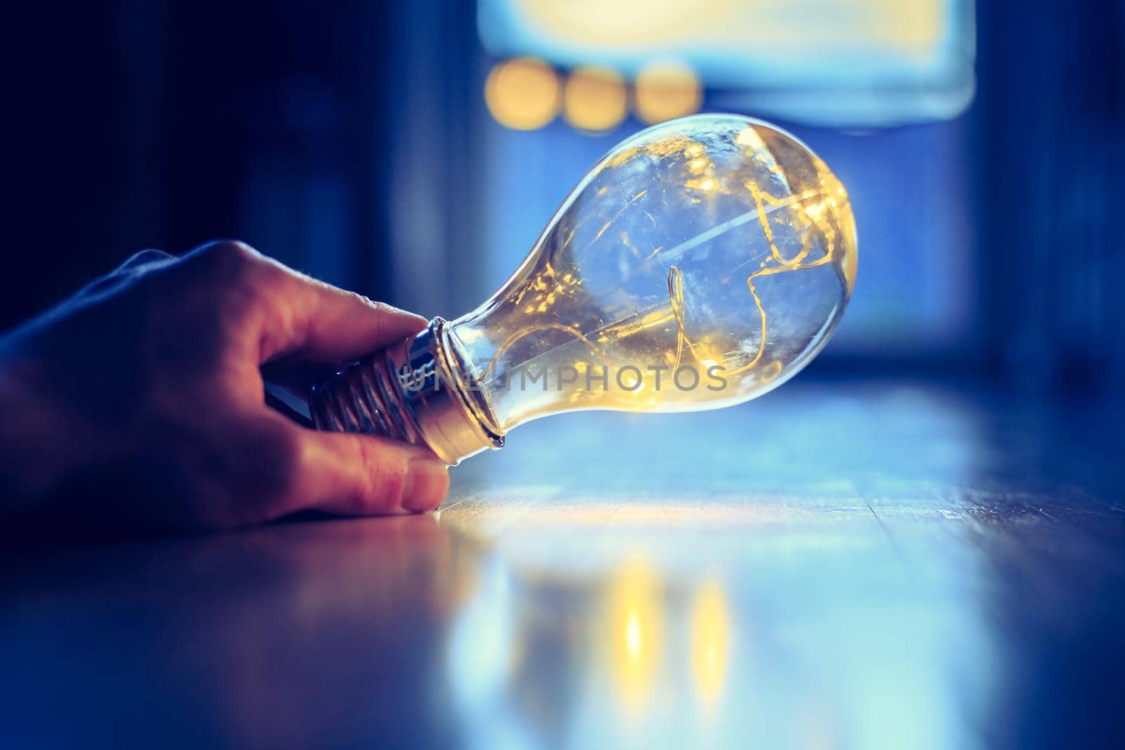 Hands are holding a LED lightbulb over the wooden floor. Symbol for ideas and innovation. Window and light in the blurry background.