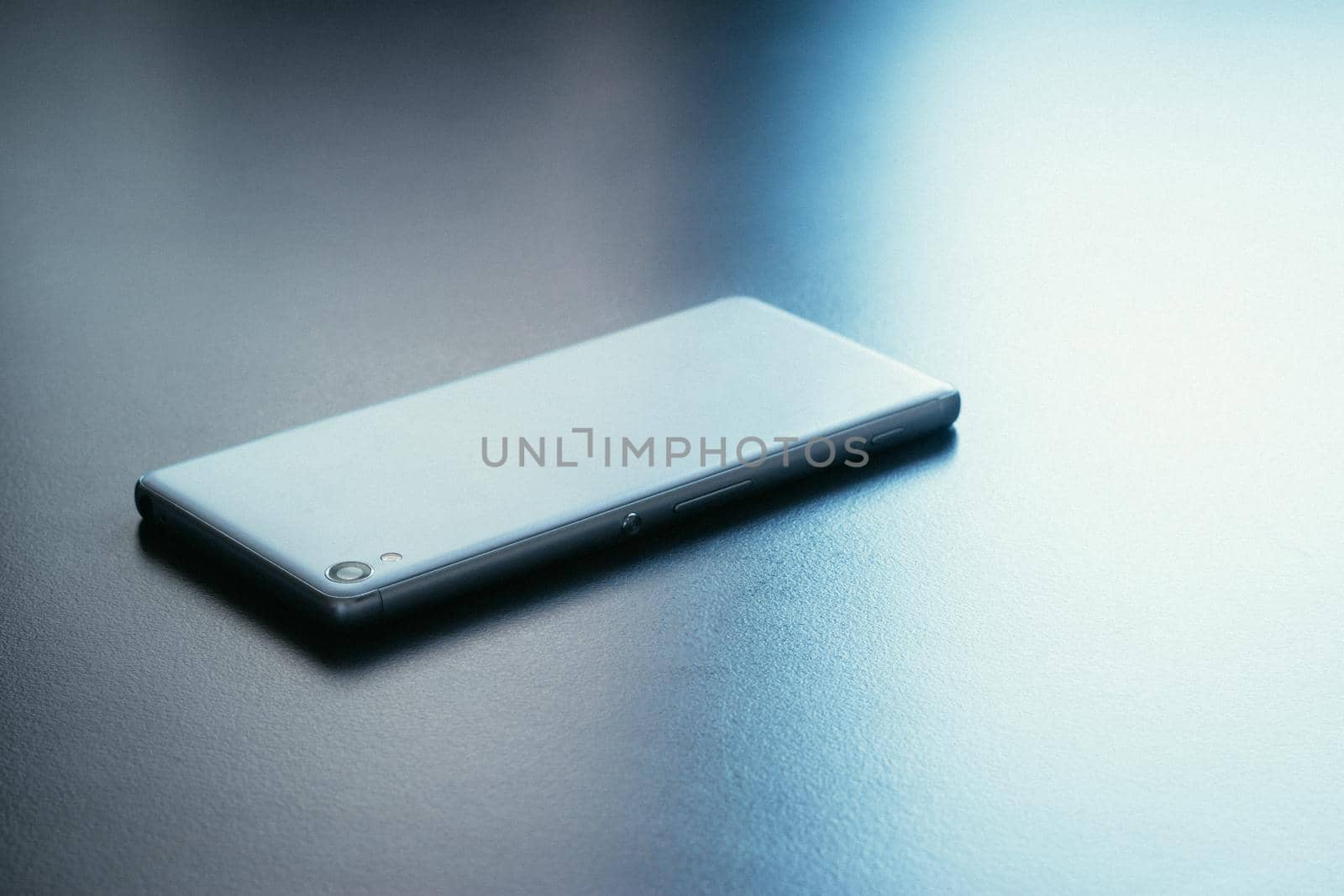 Modern white smart phone is lying on a grey surface or table, perspective view