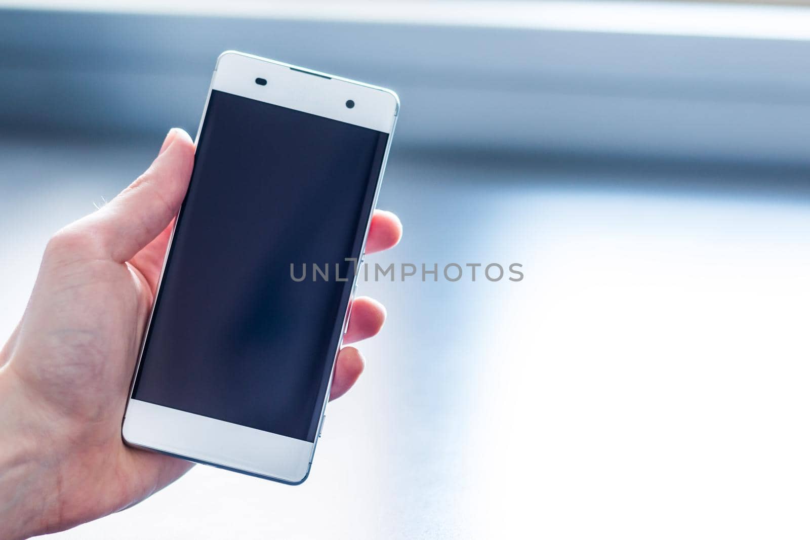 Man is holding a modern smart phone in the hand, grey desk in the background
