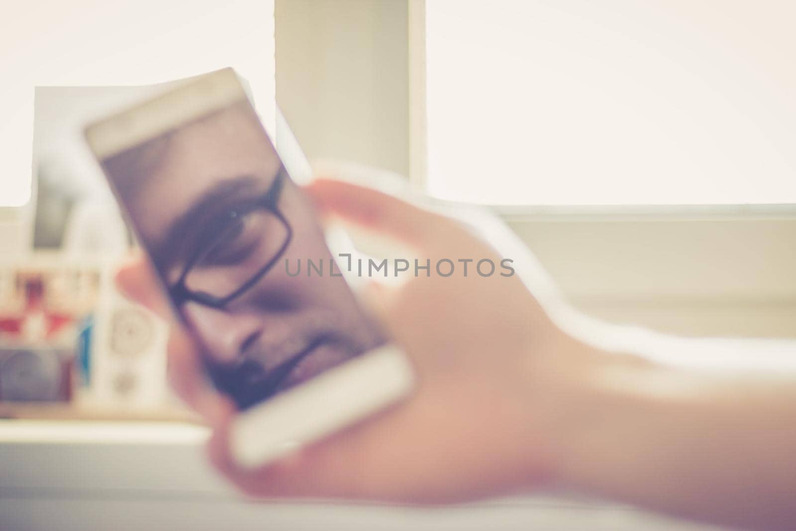 Man holds a smart phone in his hand, reflection of his face on the display