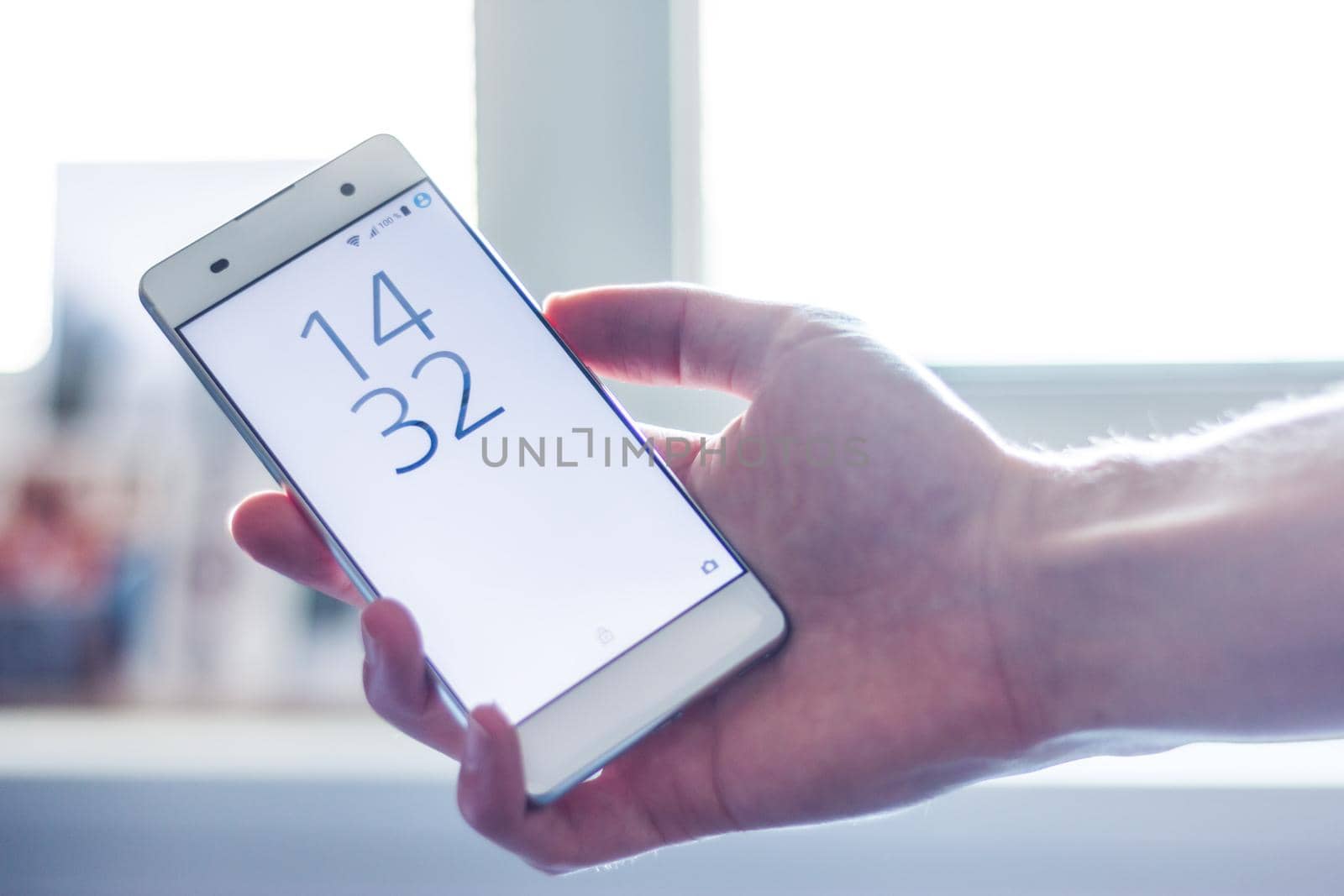 Man is holding a modern smart phone in the hand, grey desk in the background