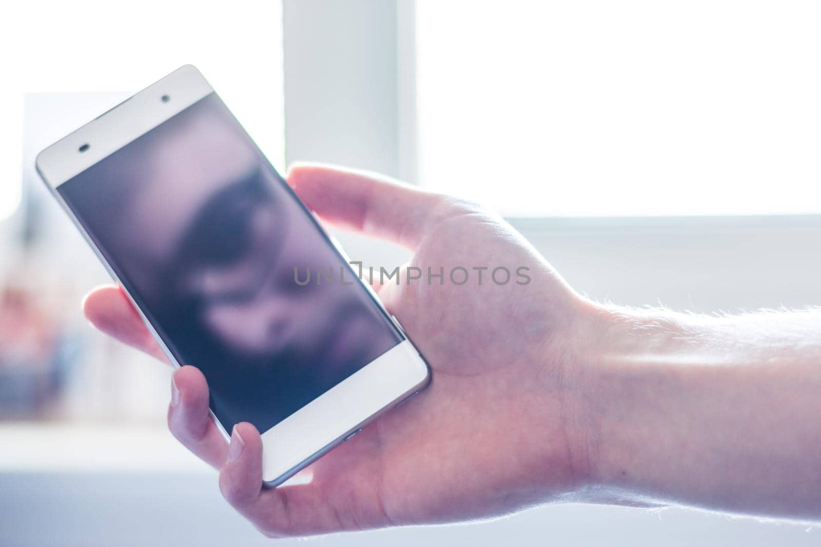 Man holds a smart phone in his hand, reflection of his face on the display