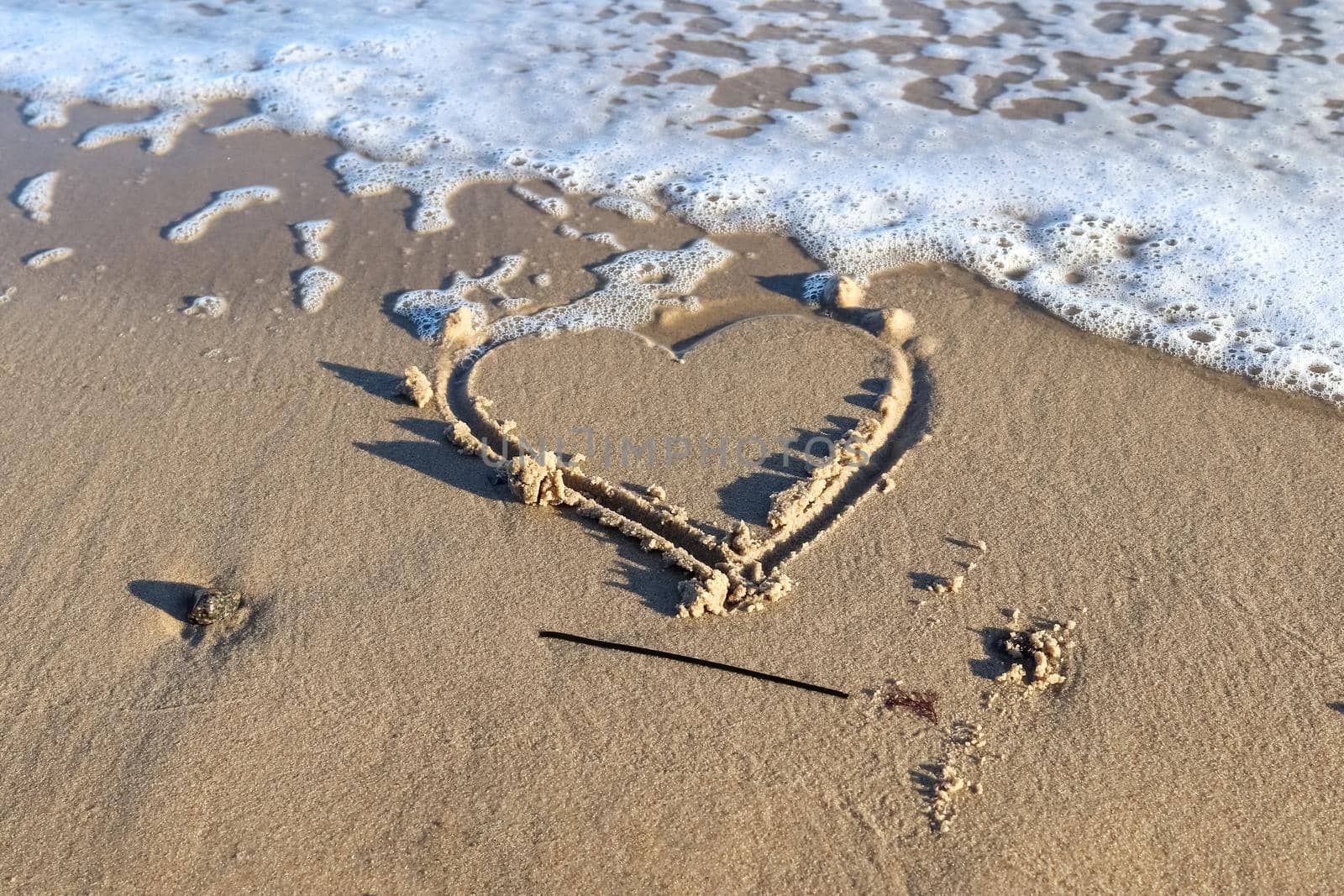 A beautiful heart shape painted into the sand of a baltic sea beach with some water waves