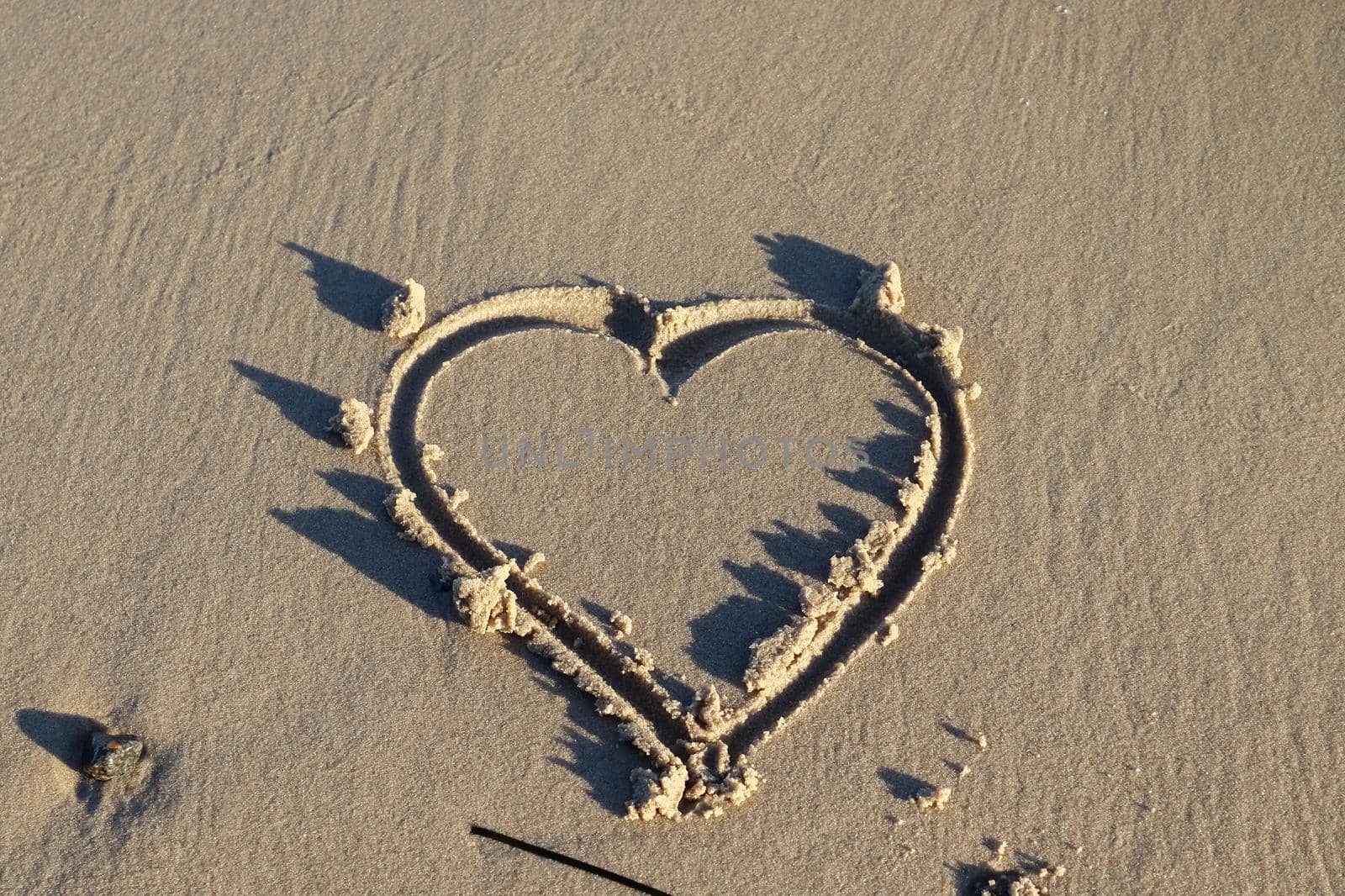 A beautiful heart shape painted into the sand of a baltic sea beach with some water waves