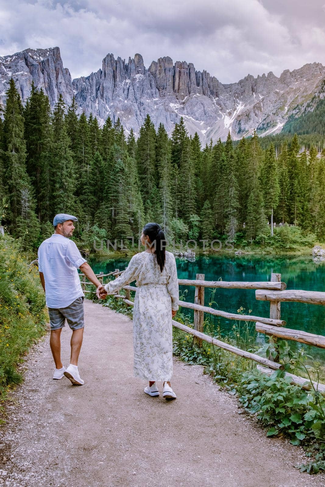 couple visit hte bleu lake in the dolomites Italy, Carezza lake Lago di Carezza, Karersee with Mount Latemar, Bolzano province, South tyrol, Italy. Landscape of Lake Carezza or Karersee and Dolomites in background, Nova Levante, Bolzano, Italy. by fokkebok