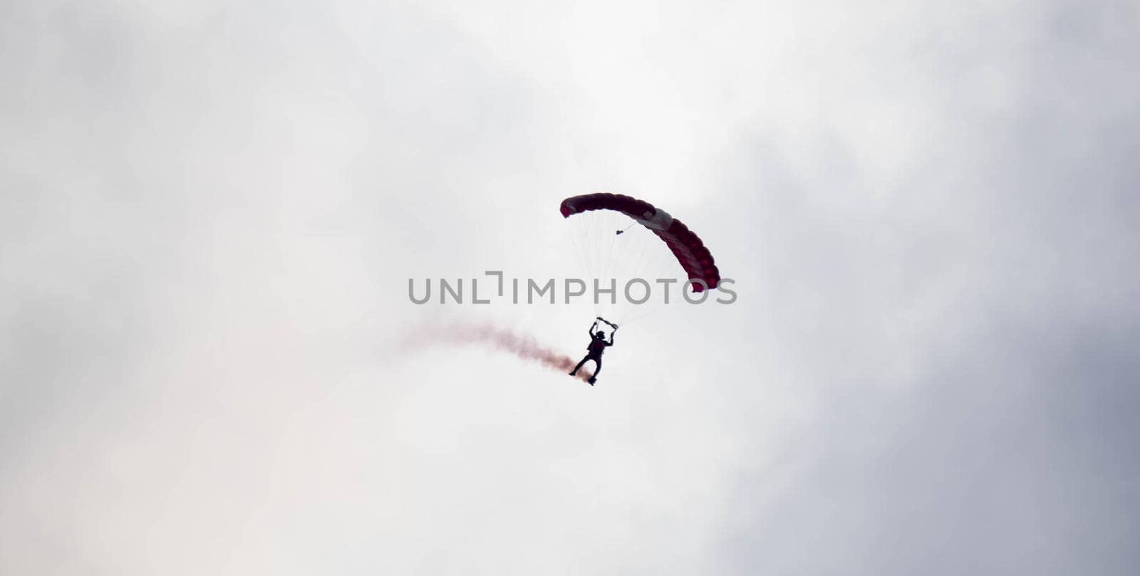 silhouette parachute stunt unfocused and blurry while gliding in the air with red smoke trail during an air exhibition in Singapore