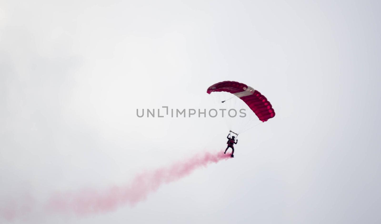 silhouette parachute stunt unfocused and blurry while gliding in the air with red smoke trail during an air exhibition in Singapore