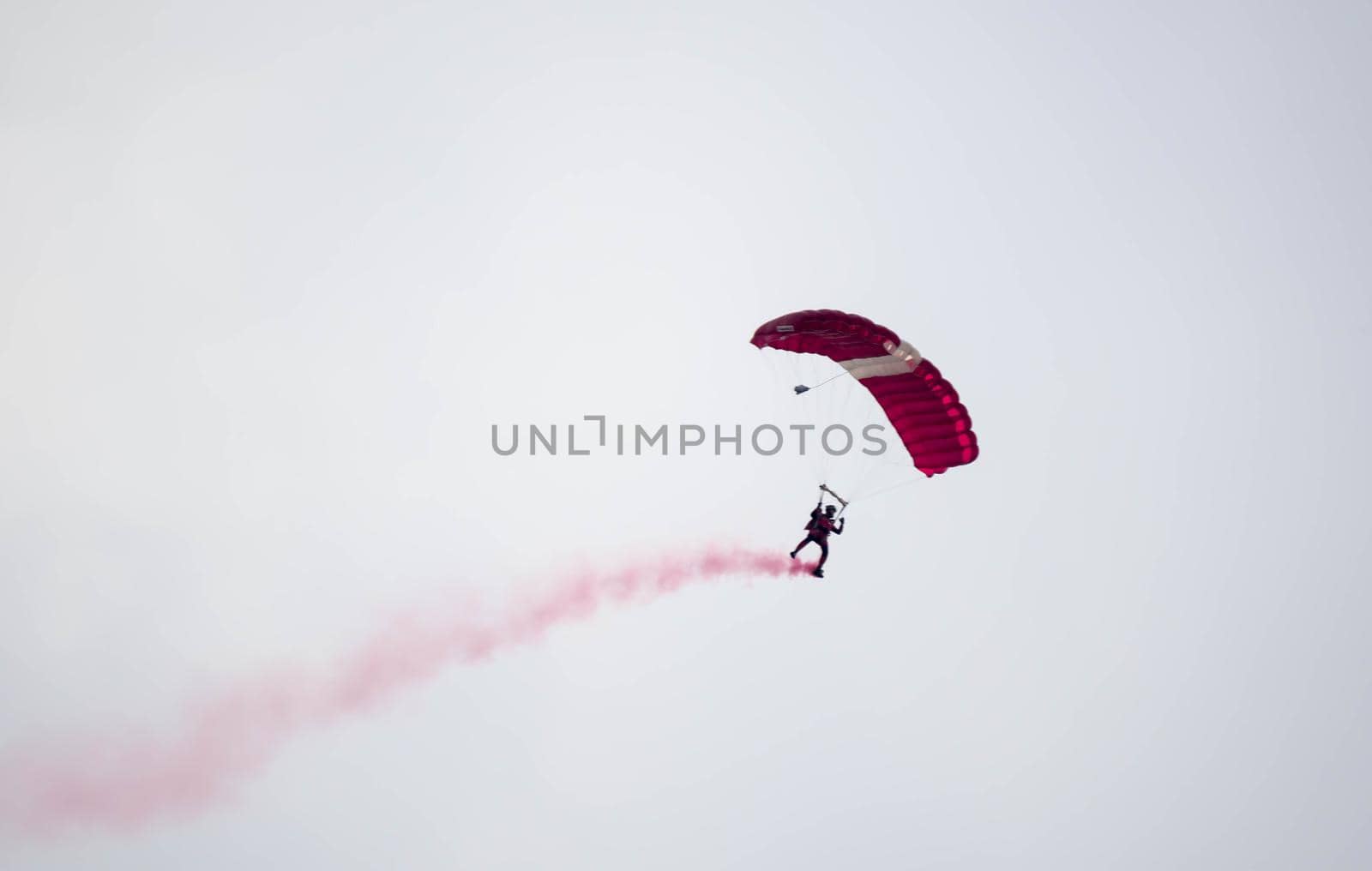 silhouette parachute stunt unfocused and blurry while gliding in the air with red smoke trail during an air exhibition in Singapore