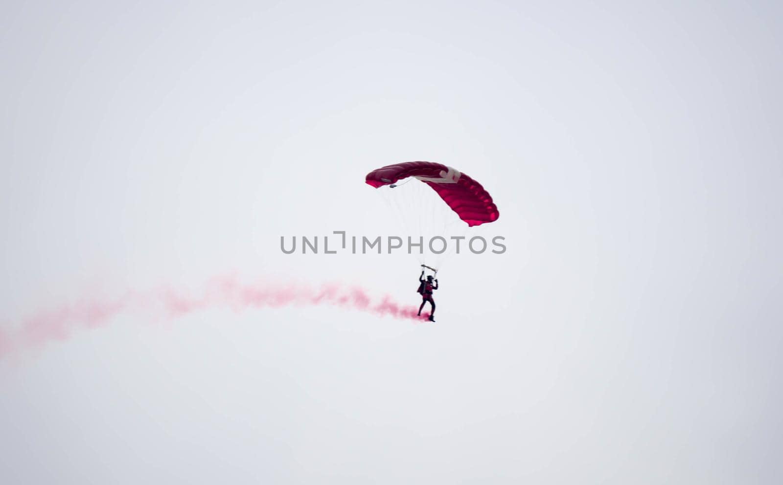 silhouette parachute stunt unfocused and blurry while gliding in the air with red smoke trail during an air exhibition in Singapore