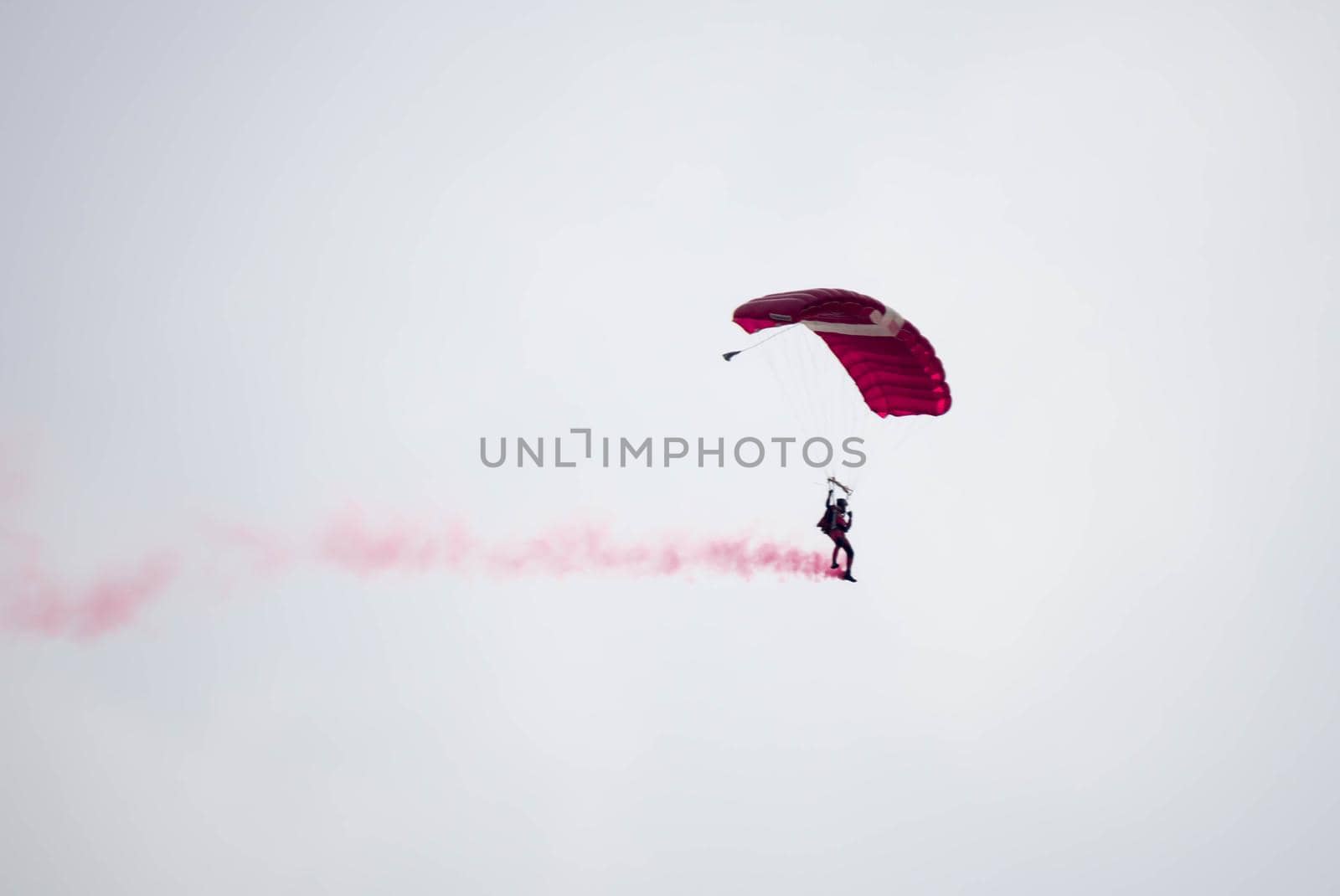 silhouette parachute stunt unfocused and blurry while gliding in the air with red smoke trail during an air exhibition in Singapore